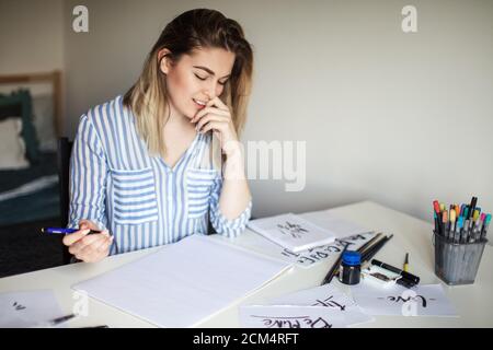 Ritratto dell'artista femminile di calligraphy pensa al lavoro mentre sedendo presso il banco dell'officina Foto Stock