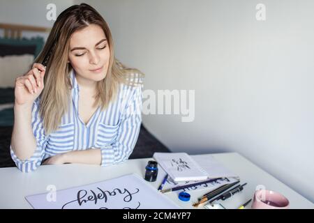 Ritratto dell'artista femminile di calligraphy pensa al lavoro mentre sedendo presso il banco dell'officina Foto Stock