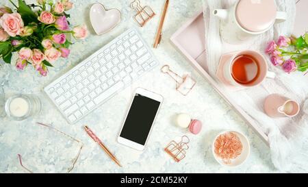 Tema rosa rossicciato accogliente spazio di lavoro da scrivania Hygge con tastiera, tè per smartphone e rosa su un elegante sfondo in marmo bianco. Vista dall'alto del blog Hero Foto Stock
