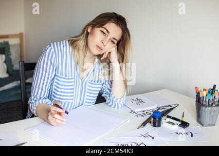 Ritratto dell'artista femminile di calligraphy pensa al lavoro mentre sedendo presso il banco dell'officina Foto Stock