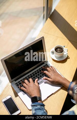 La mattina del giorno lavorativo inizia con una tazza di caffè presso il cafe e la navigazione ultime notizie in internet. Donna africana a pranzare in un caffè roastery dur Foto Stock