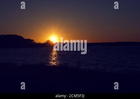 Tramonto sulla Baia di Belmont con silhouette di alberi e. scogliera Foto Stock