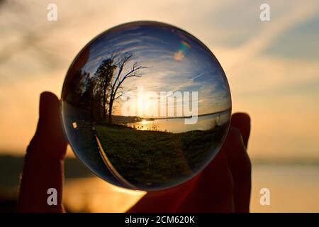 Riflesso del tramonto sull'acqua in una palla di cristallo, tenuta da una mano Foto Stock