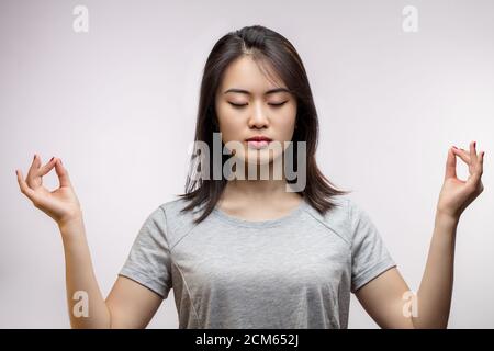 Giovane donna asiatica con occhi chiusi che si allarga le mani con gesti mudra, alla ricerca di pace in mente. Condizione di equilibrio mentale, studio isolato girato con c Foto Stock