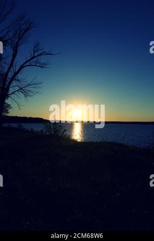 Tramonto sulla Baia di Belmont con una silhouette di alberi e scogliere Foto Stock