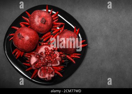 Melograno disposto su un piatto nero, su fondo grigio neutro, orizzontale Foto Stock