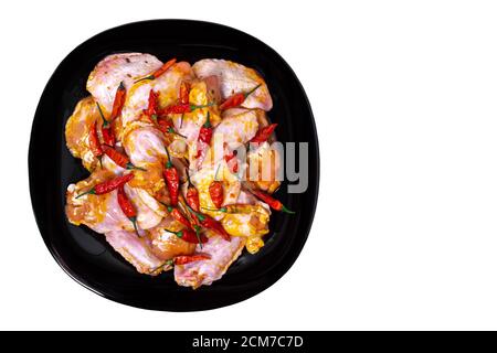 Ali di pollo crudo in una marinata con spezie su un piatto nero, un sacco di peperone rosso caldo, vista dall'alto, isolato, concetto di cibo Foto Stock