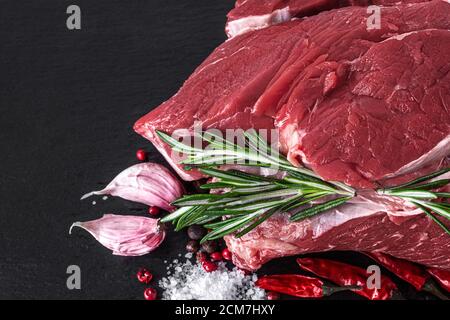 un pezzo di carne di manzo cruda su un tagliere scuro con spezie. vista dall'alto. primo piano Foto Stock