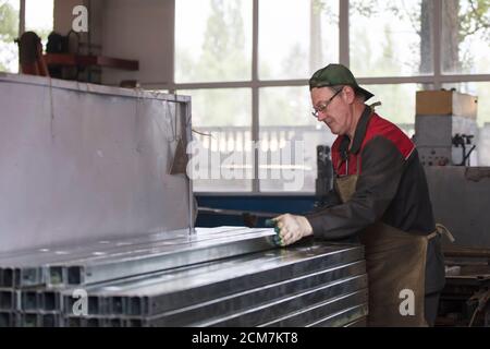 Lavoratore in un'officina con tubi di ventilazione in metallo. Foto Stock