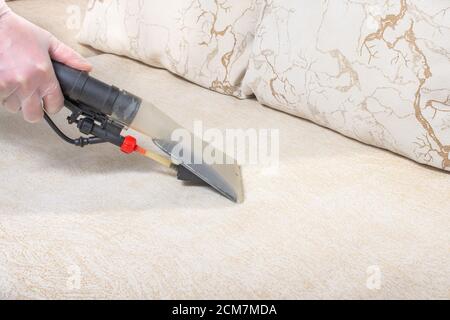 Uomo impiegato di aspirapolvere che rimuove lo sporco dai mobili in un divano piano, pulito sotto vuoto con attrezzature professionali Foto Stock