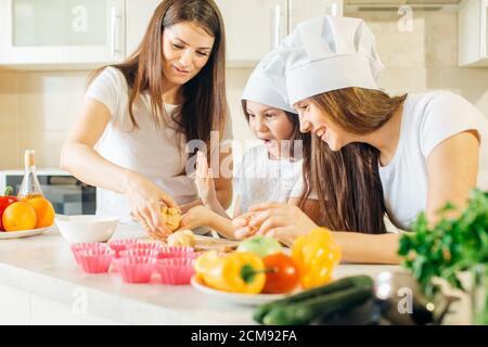 famiglia felice in cucina, madre e figlie che preparano l'impasto, cuocere i biscotti Foto Stock