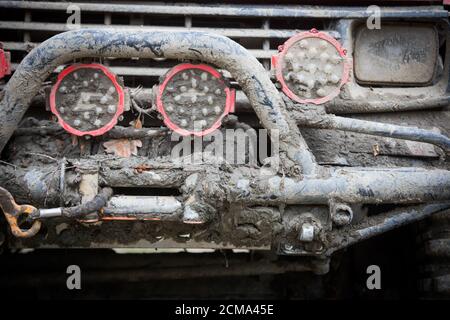 Primo piano di un'auto fuori strada, coperta di fango, con barra di carico e fari. Foto Stock