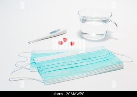Maschera medica protettiva per il viso, tre compresse rosse, termometro elettronico per la misurazione della temperatura corporea su sfondo bianco. Maschera medica per prevenire Foto Stock