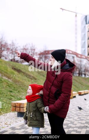 Ritratto di giovane madre e figlia che camminano all'aperto in inverno guardando via qualcosa di speciale, vista laterale Foto Stock