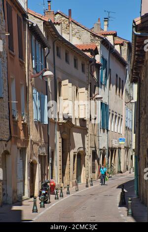 Una strada laterale illuminata dal sole che mostra i classici vecchi vani porta, le finestre e le persiane nella vecchia città di Millau, Aveyron, Francia. Una sola persona cammina in lontananza. Foto Stock