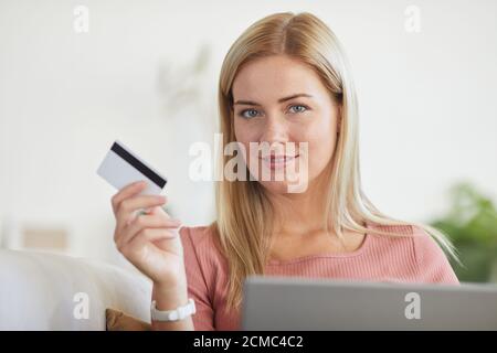 Ritratto di giovane bionda che guarda la fotocamera mentre usa portatile per pagare online con carta di credito Foto Stock