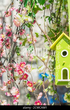 Atrificial branches of blooming cherry tree and green wooden birds house. Garden and street decoration Foto Stock