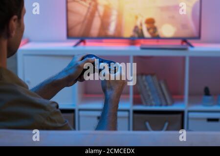 Vista posteriore di un giovane uomo che tiene il joystick e guarda la TV gioca in videogioco Foto Stock