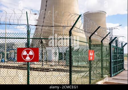 Recinzione di sicurezza di una centrale nucleare con segnali di radioattività e filo spinato e due torri di raffreddamento sullo sfondo. Foto Stock