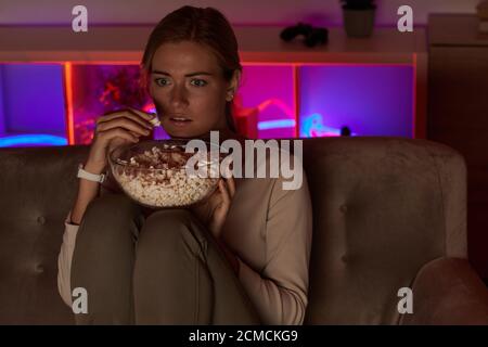 Giovane donna con spavento di popcorn durante la visione del film a casa Foto Stock