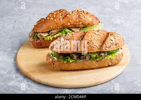 Sandwich di spratti con lattuga e formaggio cremoso su tavola di legno su fondo grigio di cemento. Vista laterale, primo piano. Foto Stock