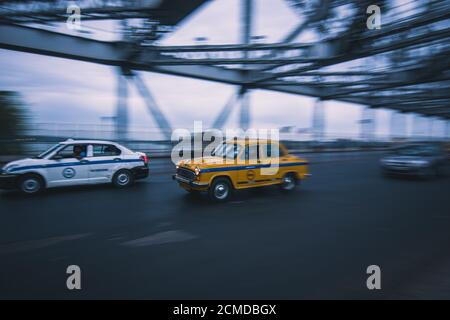 KOLKATA, INDIA - Mar 30, 2019: Un taxi Yellow Ambassador corre lungo il ponte Howrah una mattina presto. Foto Stock