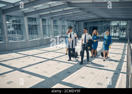 Lavoratori delle compagnie aeree con valigie di viaggio a piedi nel terminal dell'aeroporto Foto Stock