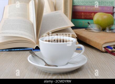 Una tazza di caffè sul tavolo contro lo sfondo di un libro aperto con un notebook Foto Stock