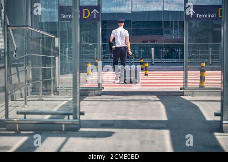 Pilota maschile con valigia di viaggio che attraversa la strada all'aeroporto Foto Stock