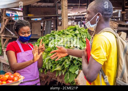 donna africana in un mercato locale che indossa una maschera facciale rifiutandosi di scuotere le mani con qualcuno Foto Stock