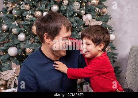 Papà e figlio si divertono, ridono e sorridono intorno all'albero di Natale. Capodanno. Foto Stock