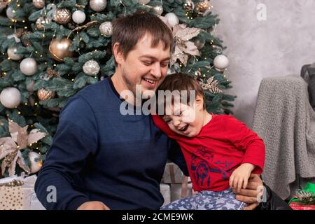 Papà e figlio si divertono, ridono e sorridono intorno all'albero di Natale. Capodanno. Foto Stock