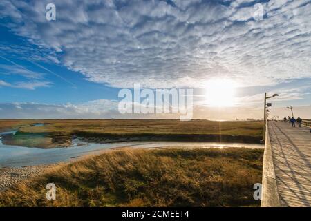 Persone irriconoscibili che camminano sulla costa di legno sulla spiaggia del mare del nord in una giornata di sole in autunno contro il cielo Foto Stock