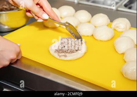 cuoco mette il ripieno in torte di carne. Le mani dello chef preparano torte di carne da vicino Foto Stock