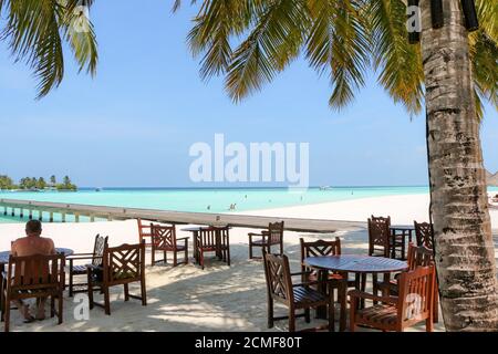 Romantico ristorante esterno tavolo e sedie sulla spiaggia il tramonto con foglie di palmo Foto Stock