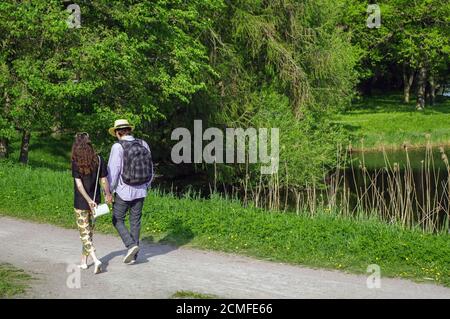 Felice giovane coppia che cammina nel parco estivo con le mani un laghetto sul lato Foto Stock