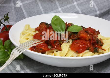 Pasta Tagliatelle con pomodori prugne freschi e basilico su un piatto bianco. Un asciugamano rustico da cucina, pomodori e foglie di basilico sullo sfondo Foto Stock