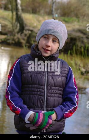 closeup ritratto di una ragazza in piedi nel parco vicino stagno in primavera, indossando cappello, guanti e piegato Foto Stock