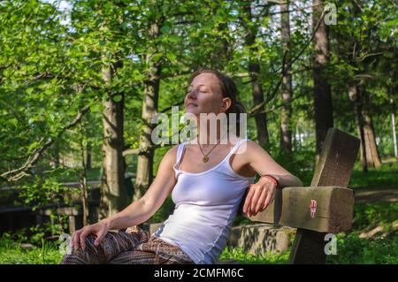 giovane donna felice seduta all'aperto su panca e rilassante con occhi chiusi Foto Stock