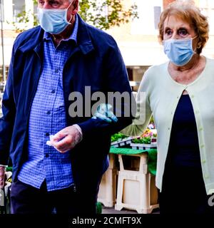 Coppia anziana braccio da passeggio nel braccio che indossa maschere per il viso durante COVID-19 Pandemico Foto Stock