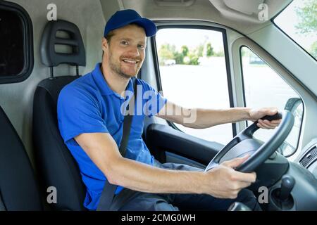 servizi di trasporto - giovane autista di sesso maschile in uniforme blu che guida un furgone. sorridendo alla macchina fotografica Foto Stock