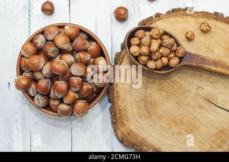 Le nocciole in una ciotola vicino a un cucchiaino di noce sbucciata su una superficie in legno Foto Stock