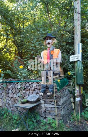 Vista insolita a grandezza naturale sulla corsia di campagna vestita con cappottatura e seduta eremita scarecrow indossando divisa intelligente nel giardino di fronte vendere verdure Foto Stock