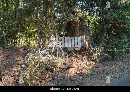 Vista insolita a grandezza naturale sulla corsia di campagna vestita su strada gambe di scarrecrow incidentate appese fuori dalla banca e schiacciate mountain bike Foto Stock