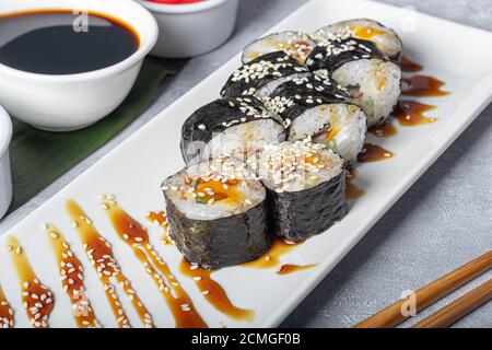 Sushi Imposta nigiri, Uramaki, California, Philadelphia, su un piatto bianco. Zenzero e wasabi nelle vicinanze. Salsa di soia in un recipiente bianco. Su uno sfondo grigio chiaro Foto Stock