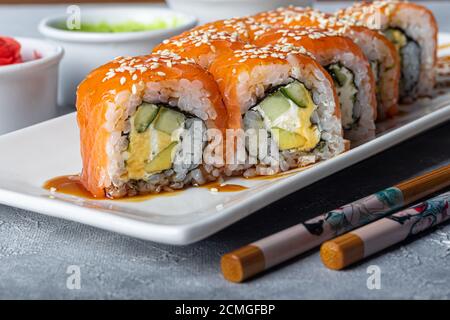 Sushi Imposta nigiri, Uramaki, California, Philadelphia, su un piatto bianco. Zenzero e wasabi nelle vicinanze. Salsa di soia in un recipiente bianco. Su uno sfondo grigio chiaro Foto Stock