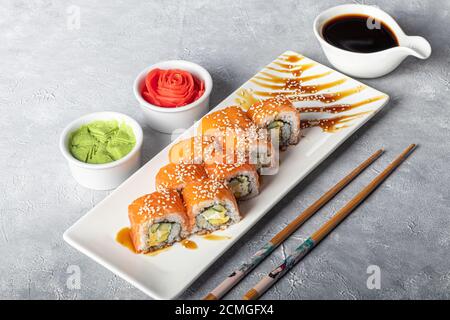 Sushi Imposta nigiri, Uramaki, California, Philadelphia, su un piatto bianco. Zenzero e wasabi nelle vicinanze. Salsa di soia in un recipiente bianco. Su uno sfondo grigio chiaro Foto Stock