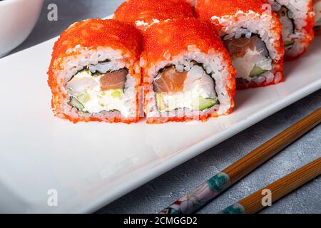 Sushi Imposta nigiri, Uramaki, California, Philadelphia, su un piatto bianco. Zenzero e wasabi nelle vicinanze. Salsa di soia in un recipiente bianco. Su uno sfondo grigio chiaro Foto Stock