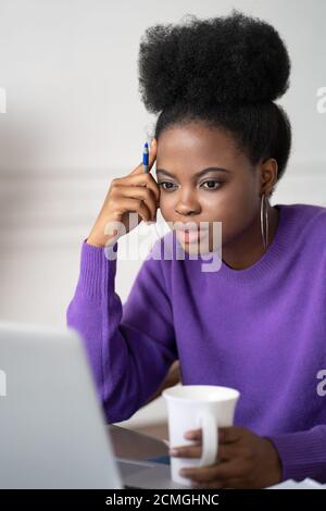 Donna studentesca afro-americana focalizzata con lezione di ascolto afro-acconciatura, guardando il webinar su laptop, studiare online, prepararsi per l'esame, ho Foto Stock