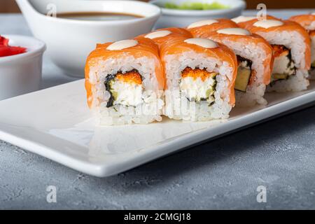 Sushi Imposta nigiri, Uramaki, California, Philadelphia, su un piatto bianco. Zenzero e wasabi nelle vicinanze. Salsa di soia in un recipiente bianco. Su uno sfondo grigio chiaro Foto Stock